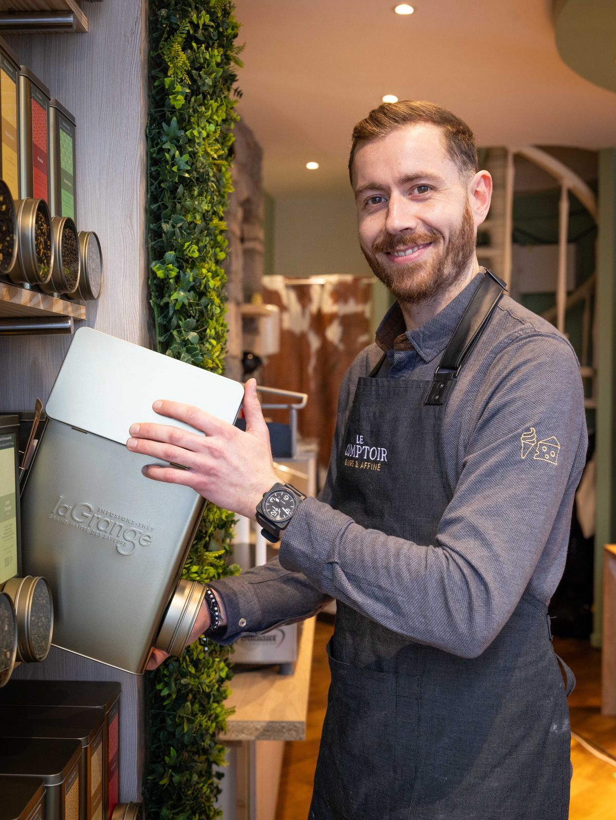 Au rayon thés du Comptoir, en tablier brodé, un grand sourire et une boîte de thé à la main