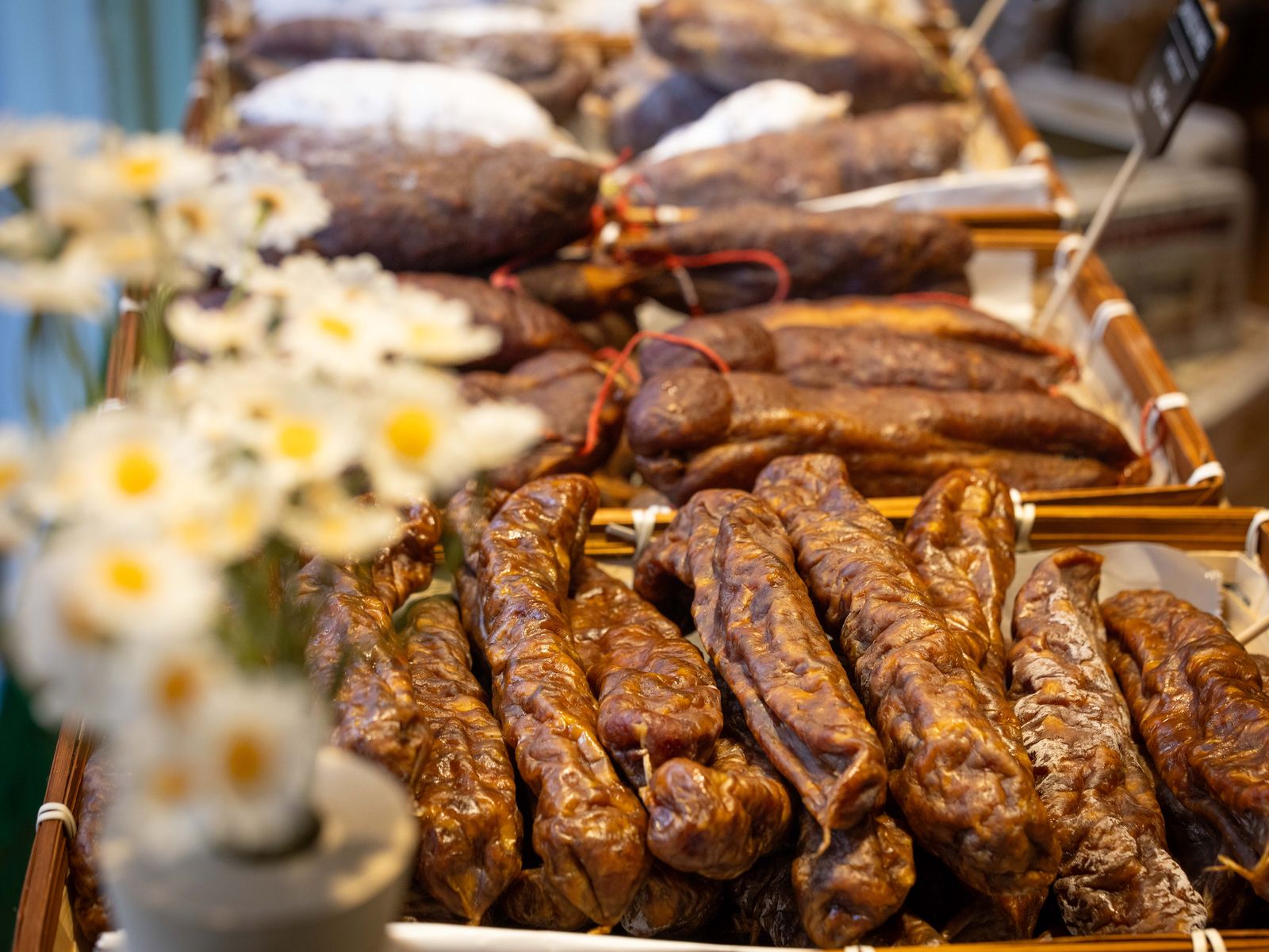 Des saucissons et des charcuteries dans des paniers, devant un bouquet de marguerites