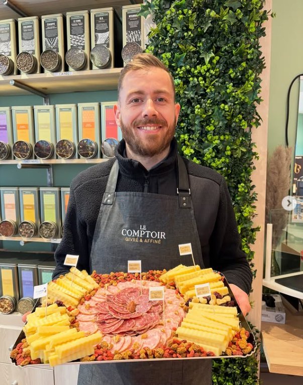 Publication Instagram : un plateau de fromages affinés, charcuteries et fruits secs tenu devant les étagères de thés
