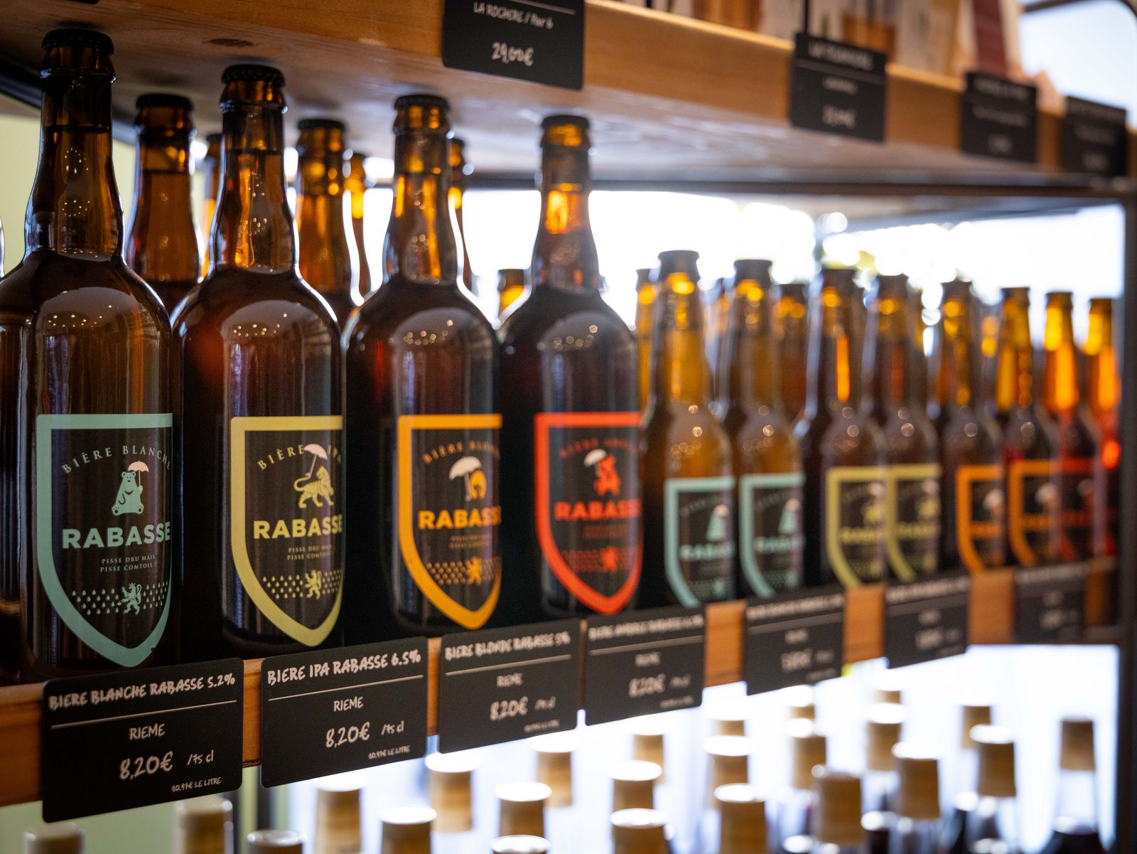 Les bières Rabasse alignées sur l'étagère : blanche, IPA, blonde et ambrée, avec leurs ardoises de prix